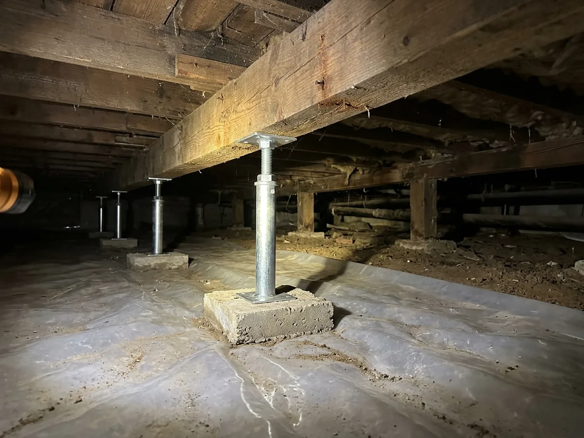 Steel adjustable support posts on new concrete pads under a sagging wood beam in a crawl space