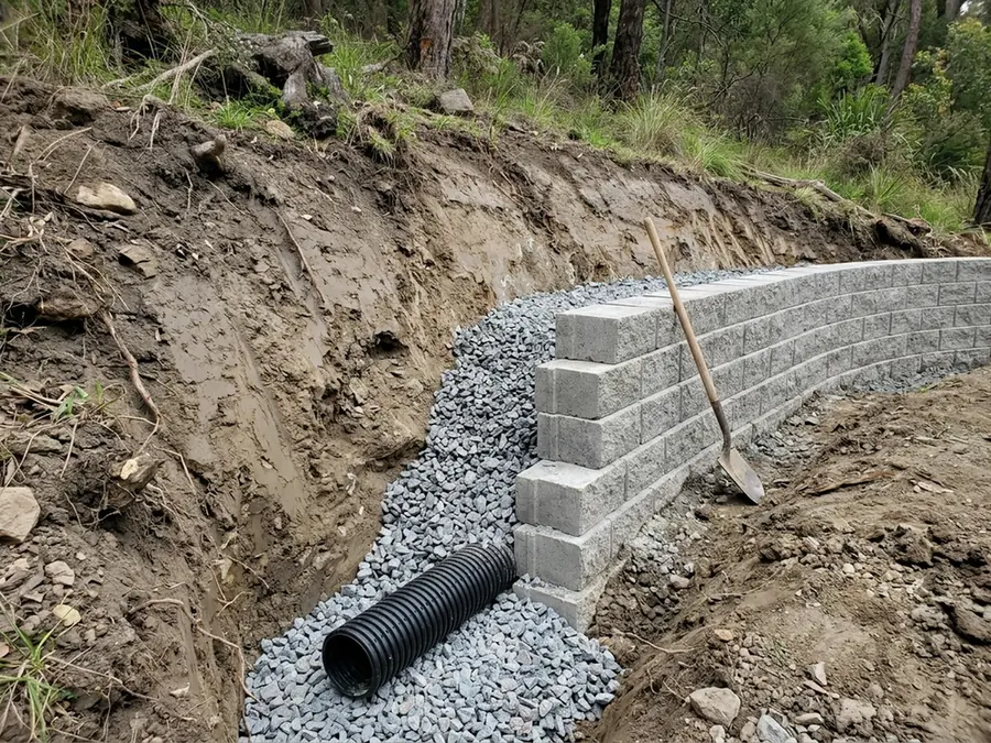 Excavated space behind a retaining wall with a perforated drain pipe laid in clean crushed stone backfill