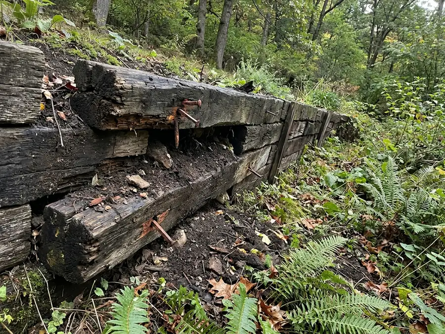 Old timber landscape-tie retaining wall leaning forward with rotted ends and soil spilling between the ties